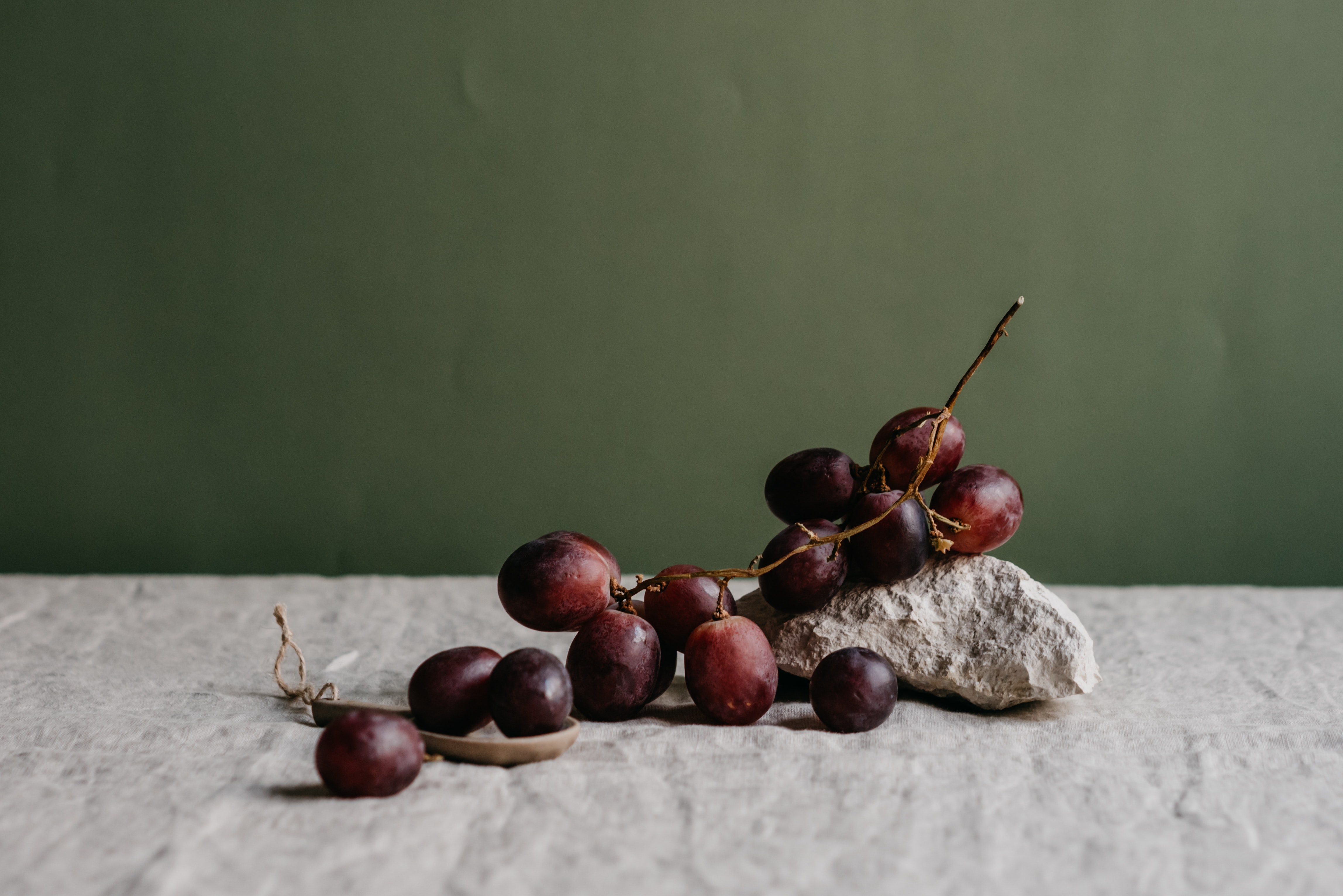 Red grapes sitting on a gray marbled countertop, in front of a dark green background.