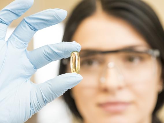 Female scientist examining omega-3 capsule.