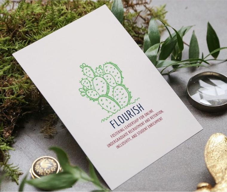 A white card with the FLOURISH logo rests on a table with greenery