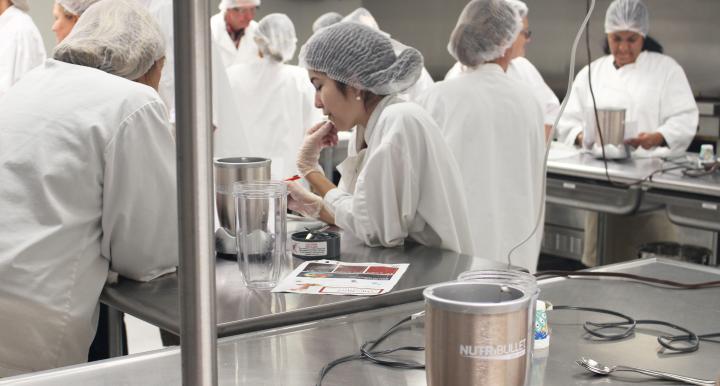 Several college students wearing white coats and hair nets work in an industrial kitchen.