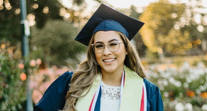 Natalie Jimenez wears a cap and gown and poses in front of a rose garden